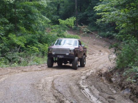 1980 Ford Bronco - A brown Ford pickup truck navigates a muddy, wooded trail.
