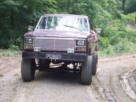 1980 Ford Bronco - This maroon Ford truck features a distinctive grille and "FORD" badging, seen from the front on a dirt road.