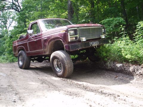 1980 Ford Bronco - Maroon Ford Bronco navigating a dirt path in a wooded area.