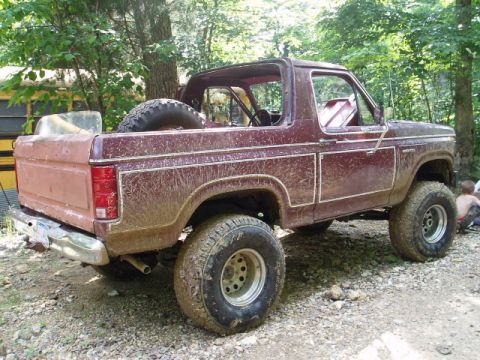 1980 Ford Bronco - This muddy maroon Ford Bronco is viewed from a three-quarter front angle, showing its off-road condition.