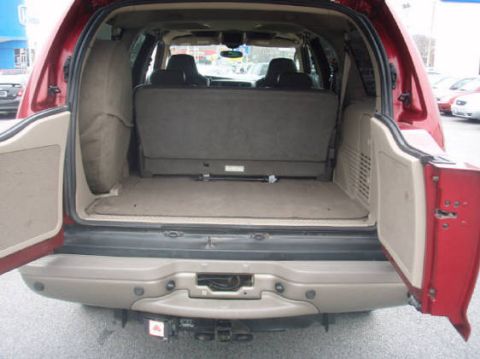 2003 Ford Excursion - The spacious cargo area of a red SUV is visible with the rear hatch and side door open.