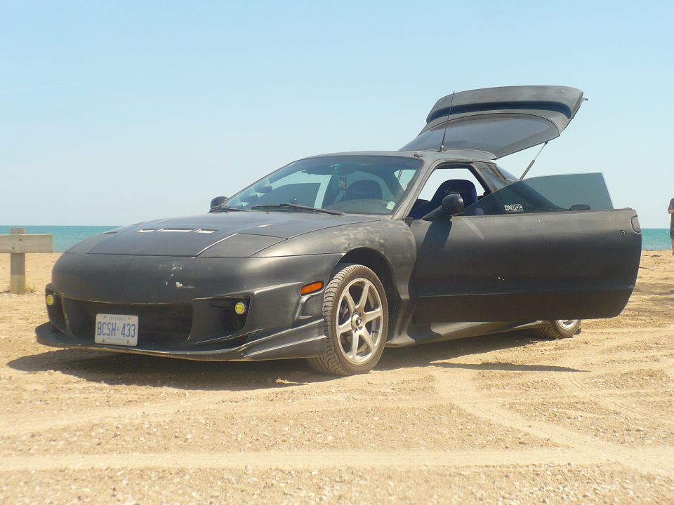 1993 Ford Probe with doors and trunk open, parked on a sandy beach near the water