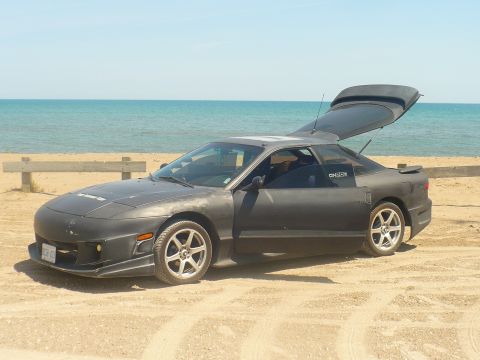 1993 Ford Probe - A 1993 Ford Probe sits on the sand near the ocean, with its trunk and driver's door ajar.