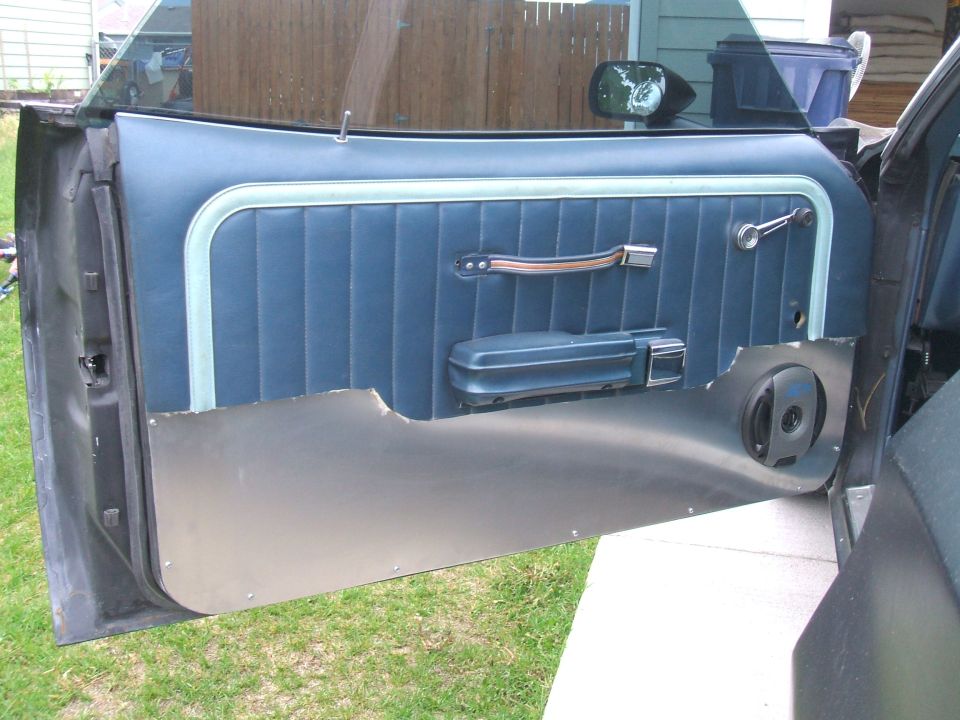Car door panel with blue upholstery, chrome handle, and speaker cutout
