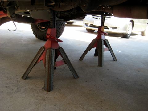 1996 Ford Bronco - A vehicle's undercarriage is raised on jack stands, with a second vehicle partially visible in the background.