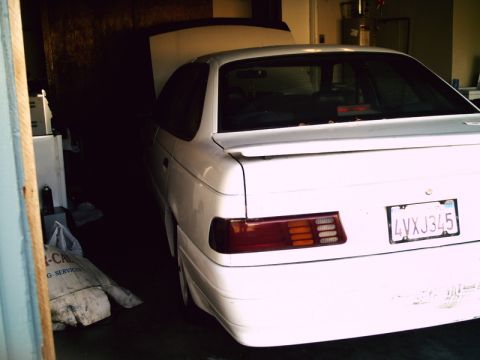 1995 Ford Taurus - The rear of a white sedan is visible, parked inside a dimly lit garage with its hood up.