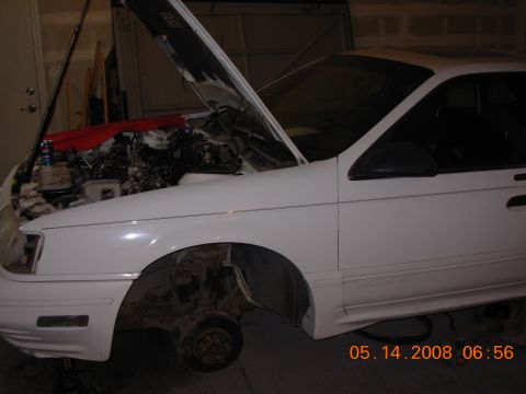 1995 Ford Taurus - A white 1995 Ford Taurus is shown with its hood open and front wheel removed, indicating it is undergoing maintenance.