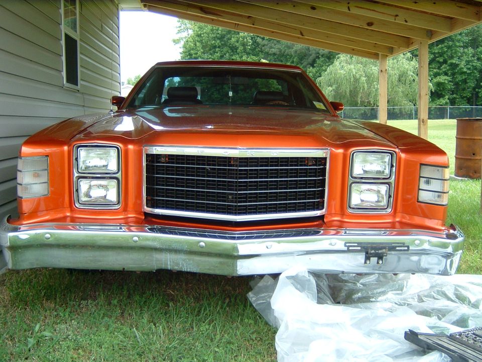 Orange 1979 Ford Ranchero front view, parked under a wooden overhang. Chrome bumper, black grille, stacked headlights