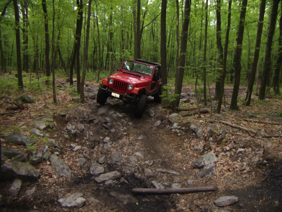 Red 2003 Jeep Wrangler navigating a steep, rocky off-road trail in a forest