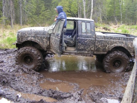 1981 Jeep CJ7 - Mud-splattered pickup truck navigates a challenging off-road terrain.
