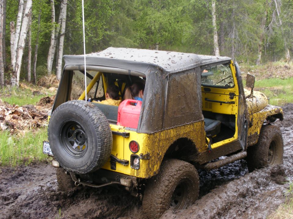 Yellow 1981 Jeep CJ7 stuck in mud, rear view with spare tire mounted