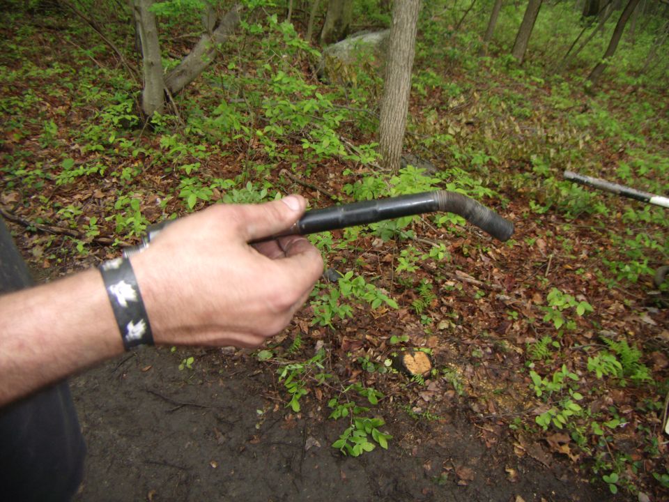 Person holding a black pipe in a wooded area.
