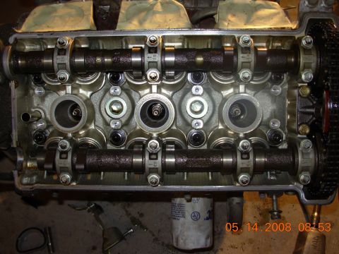 1995 Ford Taurus - The engine's cylinder head is removed, exposing the camshafts and valve train. The camshafts are lubricated with oil and are held in place…