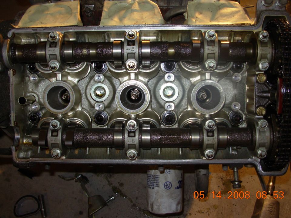 Close-up of a car engine's cylinder head with camshafts, valves, and timing chain exposed.