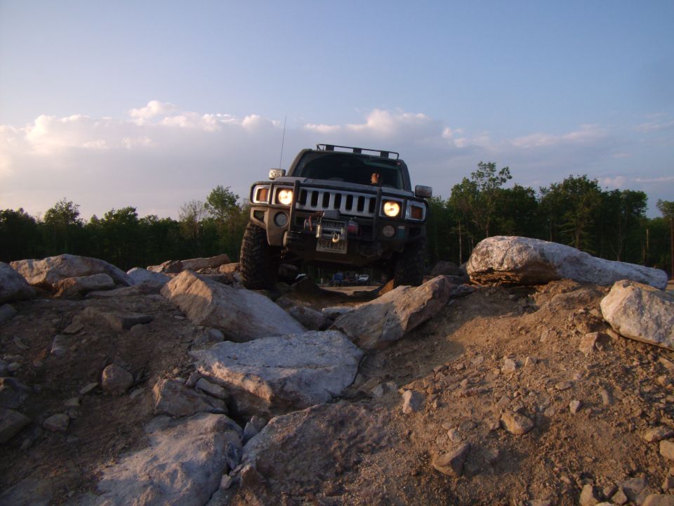 Black Hummer H2 driving over rocks on an off-road trail.