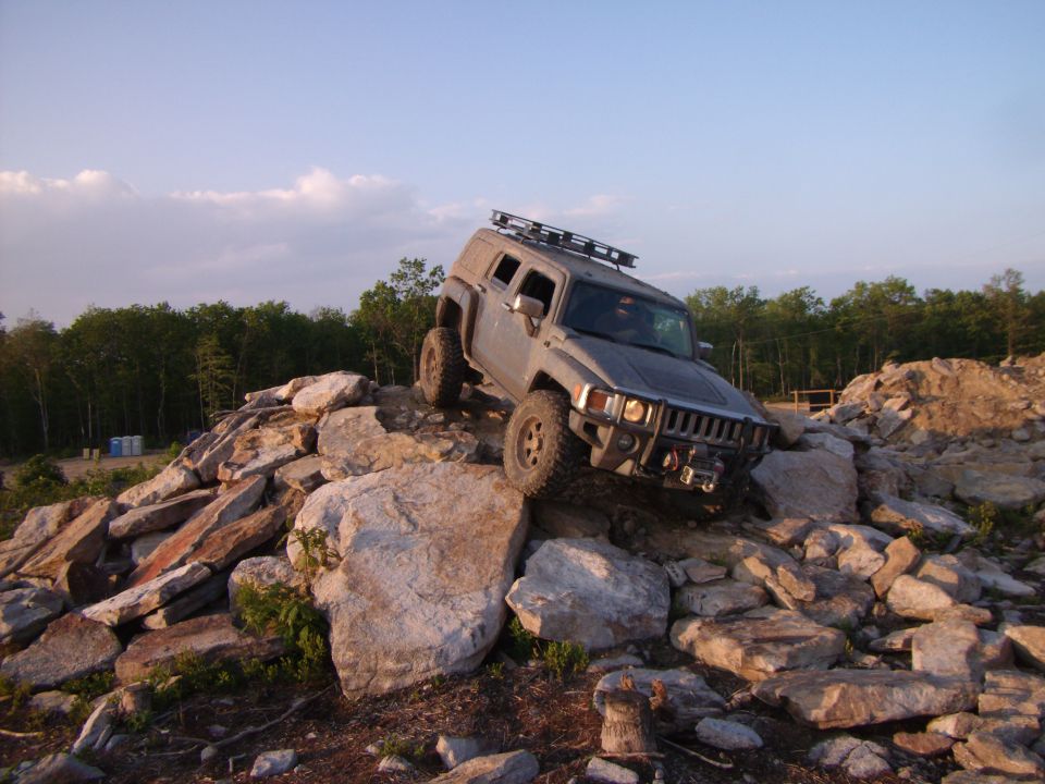 Grey Hummer H3 climbing over large rocks on an off-road trail.