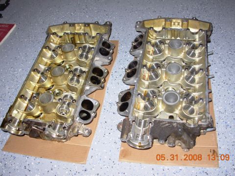 1995 Ford Taurus - Two disassembled engine cylinder heads are shown resting on cardboard on a garage floor. The heads are gold-colored and appear to be from a…