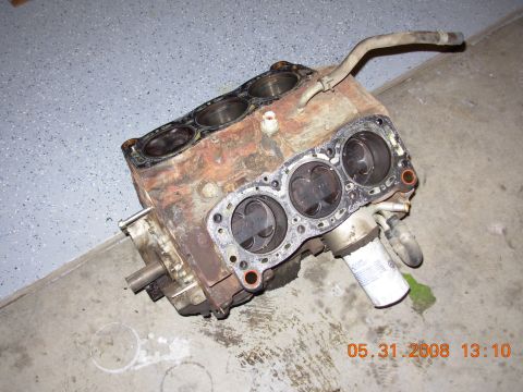 1995 Ford Taurus - A disassembled V6 engine block sits on a concrete floor. The engine block is heavily rusted and shows signs of wear, with pistons visible i…
