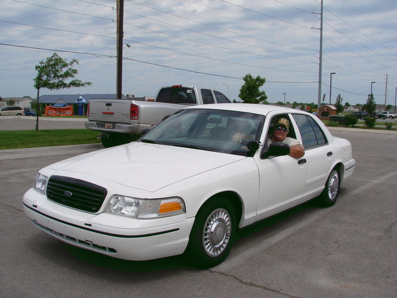 Person in a white Ford Crown Victoria, parked in a lot.