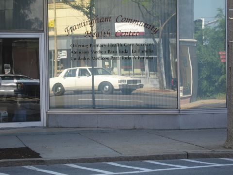 1991 Ford LTD Crown Victoria - storefront window of the Framingham Community Health Center, with a white sedan reflected in the glass.