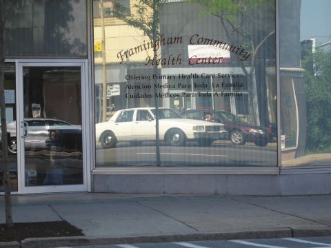 1991 Ford LTD Crown Victoria - Framingham Community Health Center storefront window reflecting a white sedan and the street outside.