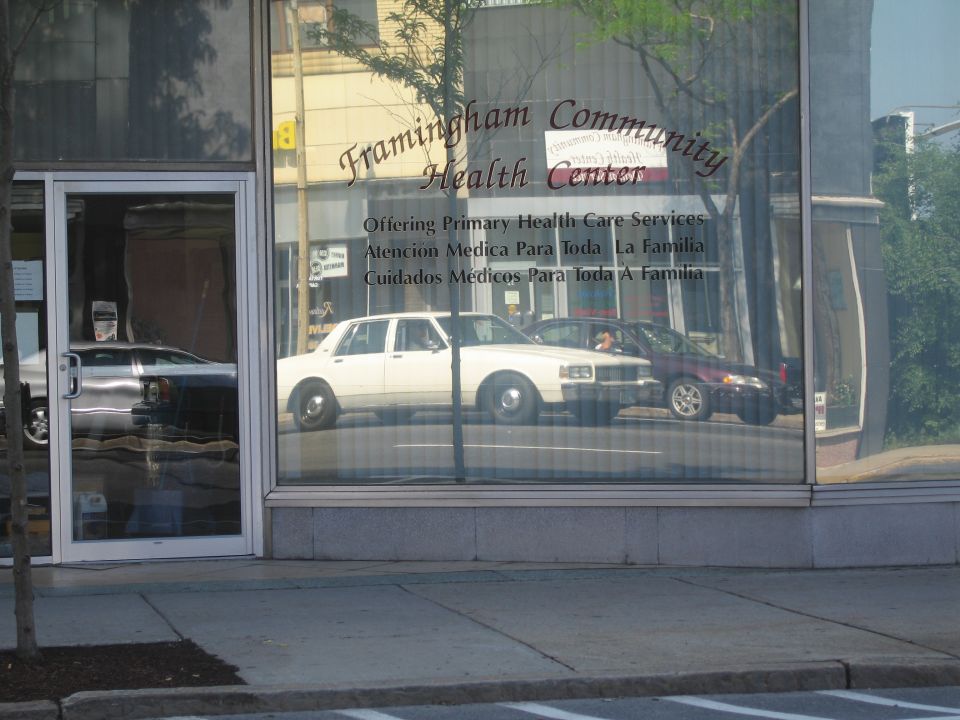 Framingham Community Health Center window reflecting a white sedan and street