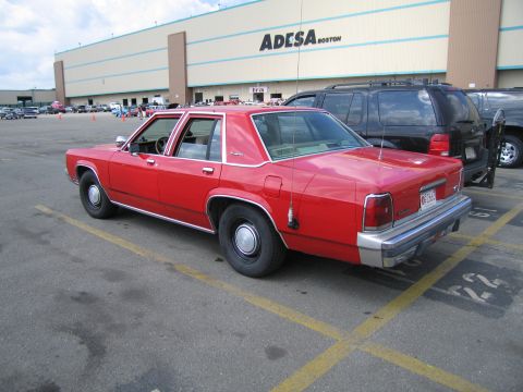 1991 Ford LTD Crown Victoria - Rear three-quarter view of a red Ford sedan in a parking lot, with a building lettered ADESA BOSTON behind.