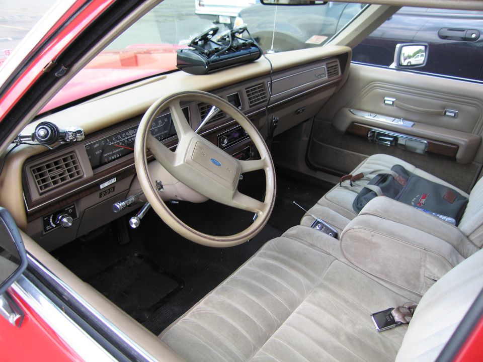 Interior of a Ford sedan with tan cloth bench seat, dash and Ford-badged steering wheel