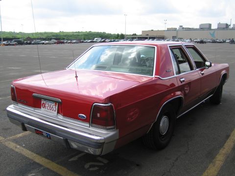 1991 Ford LTD Crown Victoria - Rear three-quarter view of a red Ford LTD Crown Victoria four-door sedan parked in a large lot.