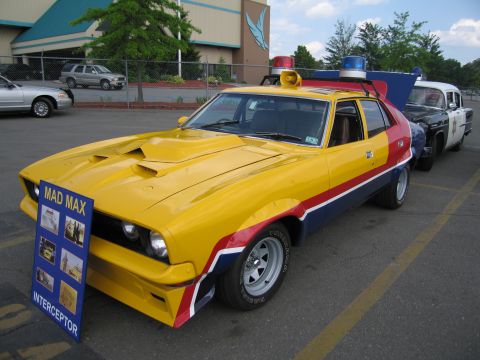 1991 Ford LTD Crown Victoria - Front three-quarter view of the yellow, red and blue Mad Max Interceptor replica with roof lights and a Mad Max display sign.