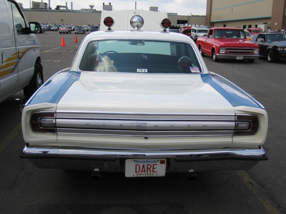 Rear of white Plymouth sedan with roof lights and DARE plate