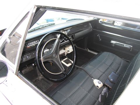 1991 Ford LTD Crown Victoria - dark dashboard, black steering wheel and cloth bench seat interior of a classic sedan viewed through the door.