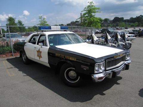 1991 Ford LTD Crown Victoria - Front three-quarter view of a black and white Deputy Sheriff sedan with star emblem and roof lights beside police motorcycles.