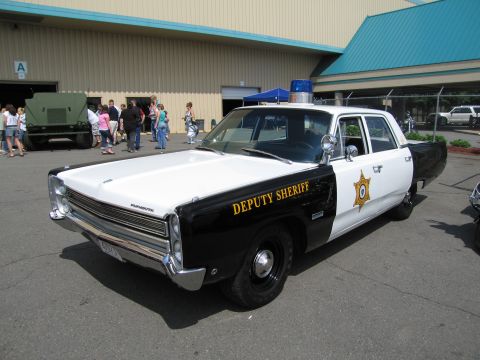 1991 Ford LTD Crown Victoria - black and white Plymouth Deputy Sheriff sedan with star emblem parked at a show with a crowd in the background.