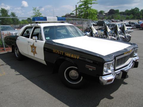 1991 Ford LTD Crown Victoria - Front passenger-side view of a black and white Plymouth Deputy Sheriff sedan with roof lights beside police motorcycles.