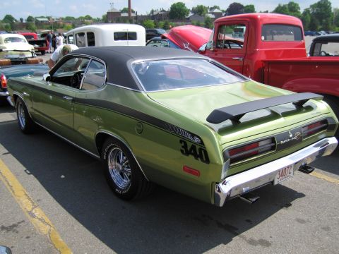 1991 Ford LTD Crown Victoria - green Plymouth Duster 340 with black side stripes and a vinyl top sits parked at an outdoor car show.