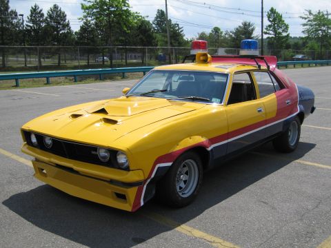 1991 Ford LTD Crown Victoria - yellow, red and grey Ford Falcon styled as a pursuit special sits in a lot with roof lights and a hood scoop.