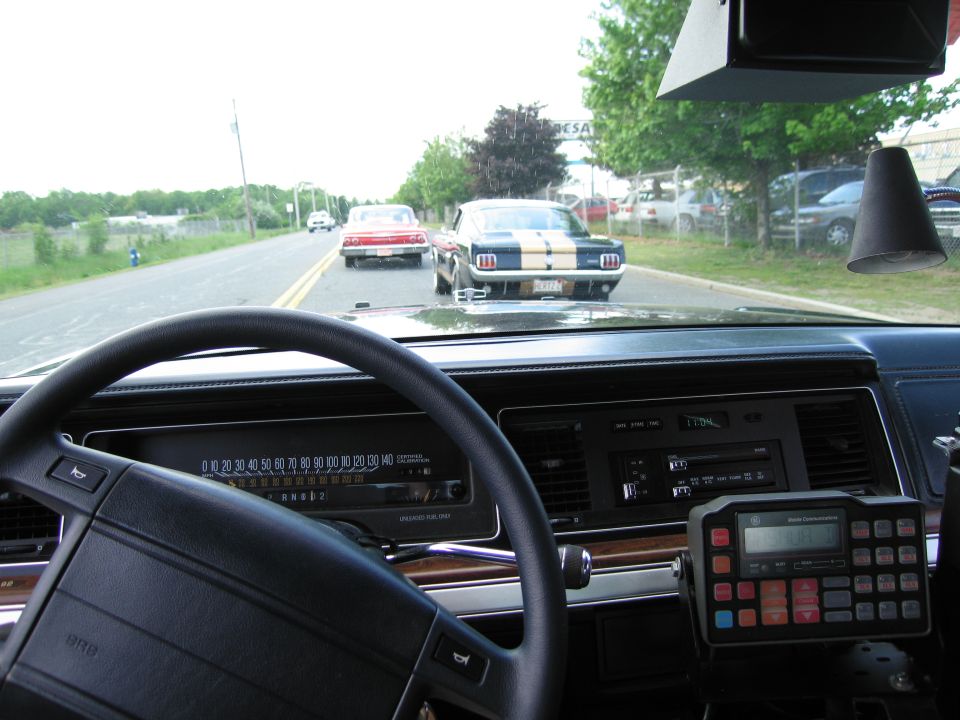 View through a car windshield of classic cars on a road, with police radio