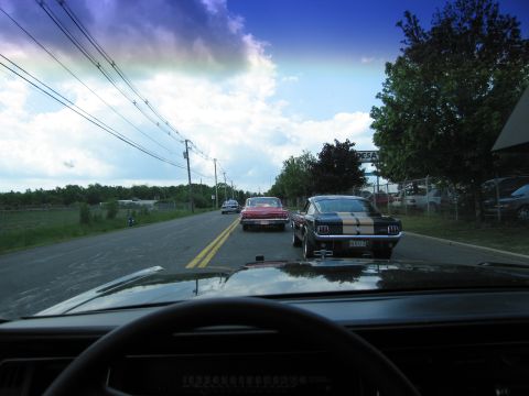 1991 Ford LTD Crown Victoria - From inside a car, a red classic and a black Mustang with racing stripes are seen ahead on a tree-lined road.