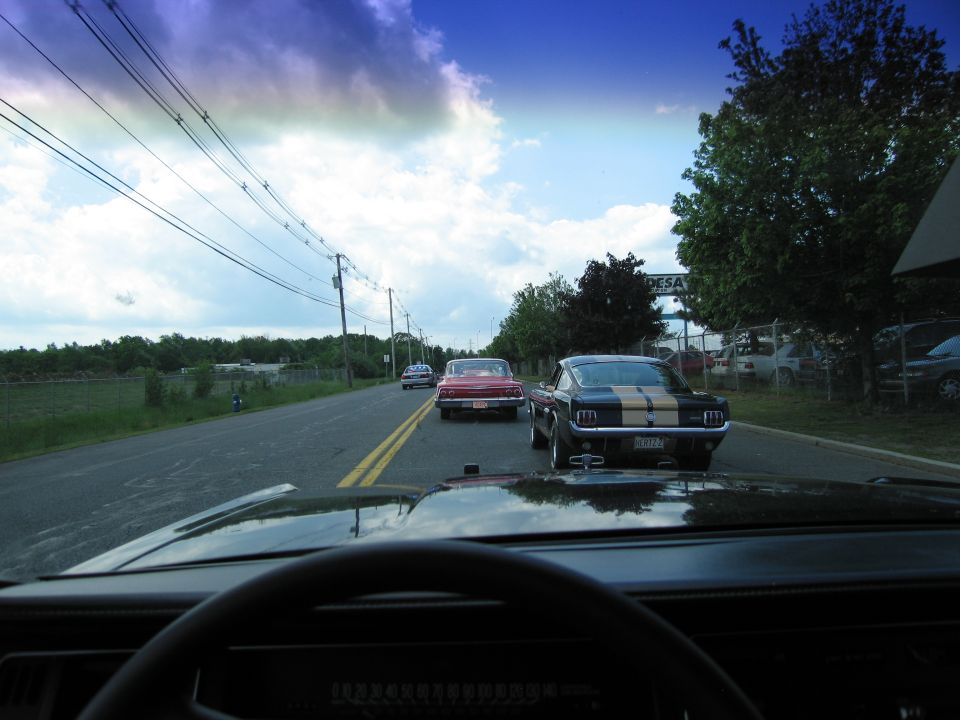 Windshield view of a red car and striped Mustang on a rural road