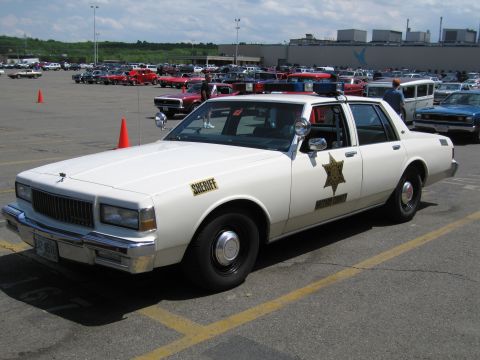 1991 Ford LTD Crown Victoria - white Chevrolet Caprice marked Hazzard County Sheriff is parked at a packed outdoor car show.