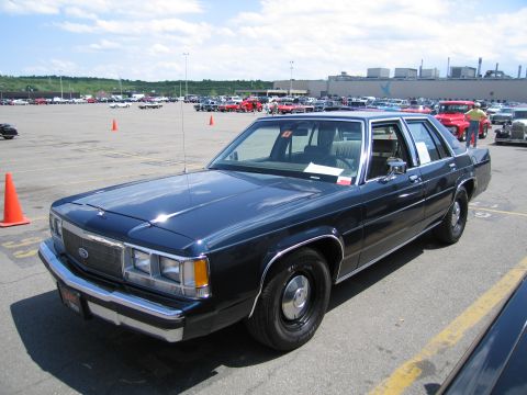 1991 Ford LTD Crown Victoria - dark blue Ford LTD Crown Victoria sedan with steel wheels is parked at a busy outdoor car show.