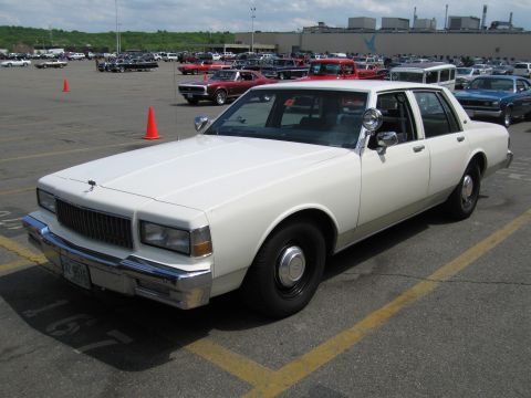 1991 Ford LTD Crown Victoria - white Chevrolet Caprice sedan sits angled in a packed car-show parking lot under a blue sky.