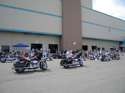 1991 Ford LTD Crown Victoria - Several Harley-Davidson touring motorcycles are parked in rows outside a large building at an outdoor event.