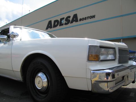 1991 Ford LTD Crown Victoria - front corner of a white Chevrolet sedan is shown against a building wall reading ADESA Boston.