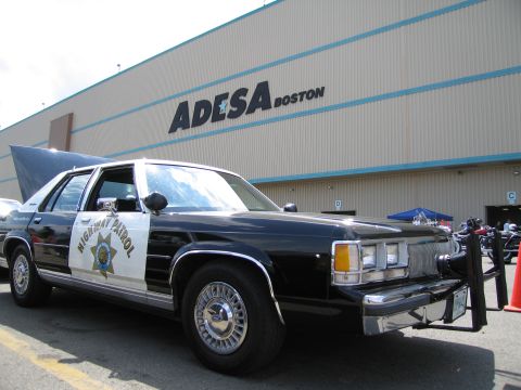 1991 Ford LTD Crown Victoria - black-and-white police sedan marked California Highway Patrol sits in a lot in front of an ADESA Boston building, trunk open.