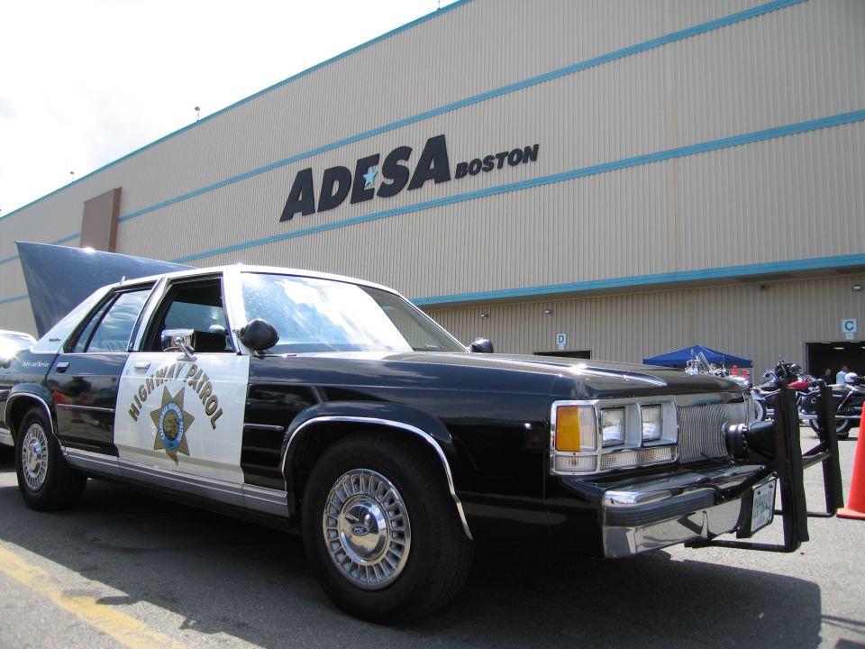 Black-and-white California Highway Patrol sedan parked outside ADESA Boston building