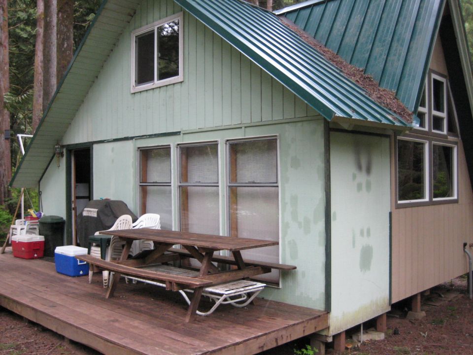 Rustic cabin with a picnic table on a wooden deck in a forest.
