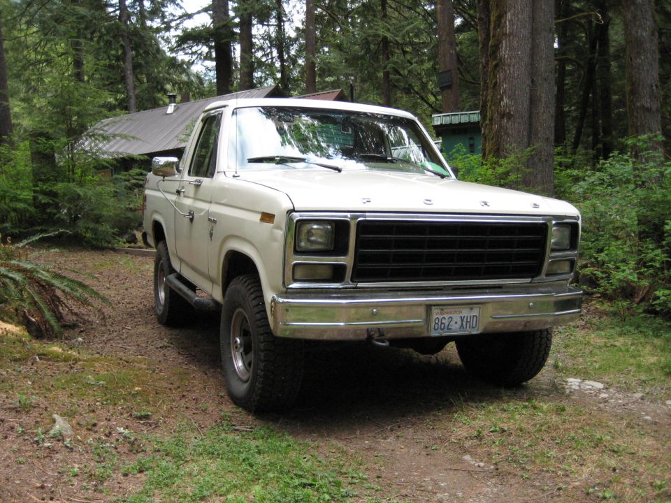 White 1980s Ford F-series pickup truck parked in a forest setting.