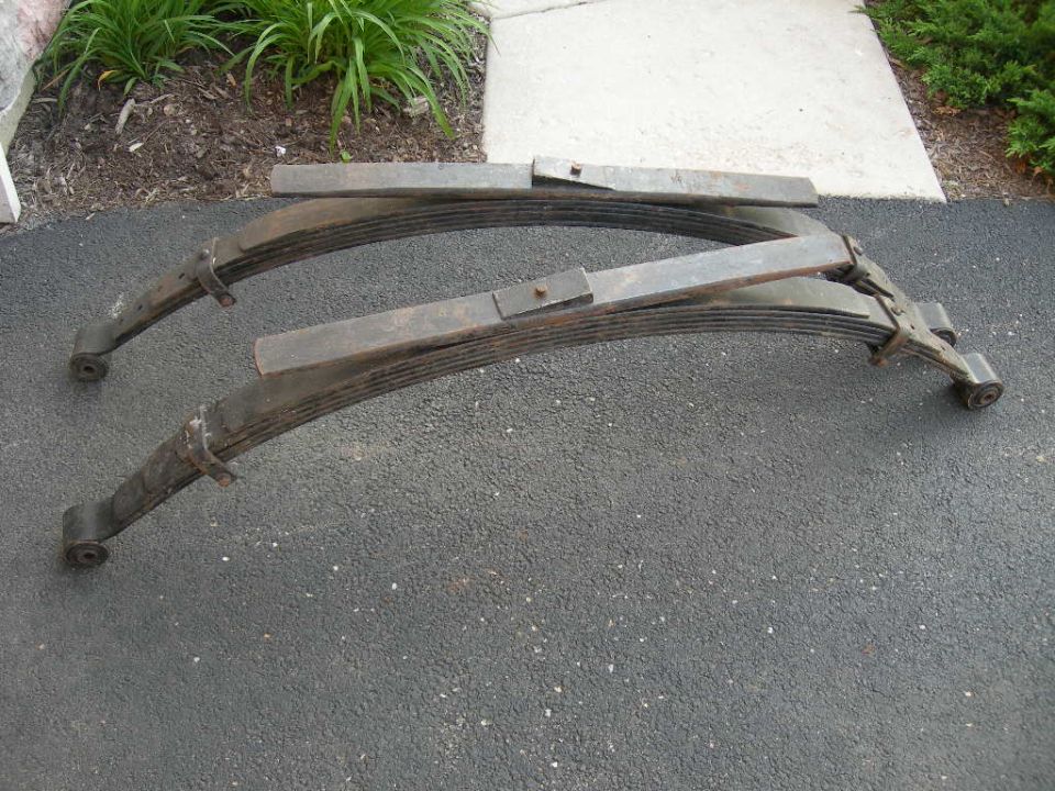 Two old, rusted leaf springs on an asphalt driveway.